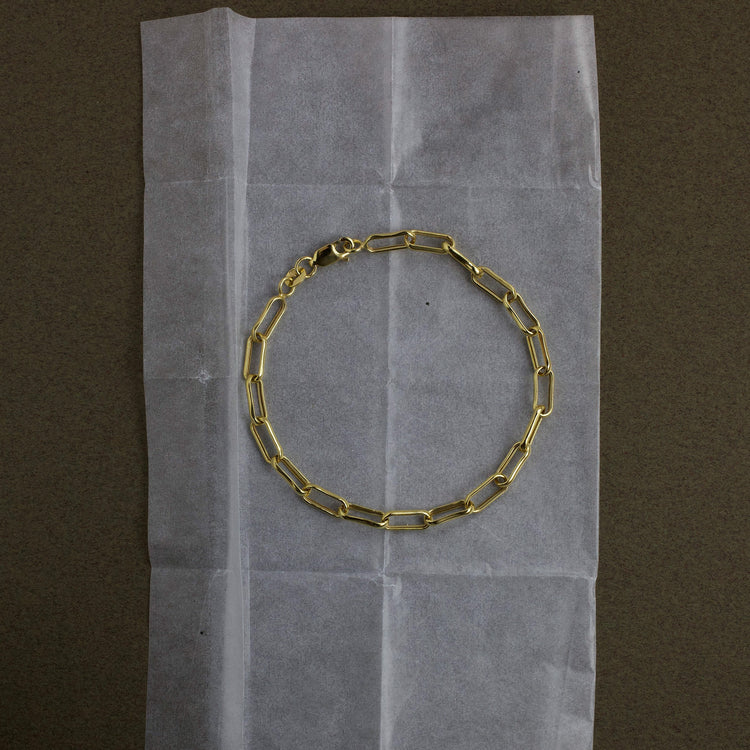 Gold chain bracelet on a piece of white paper with a brown background