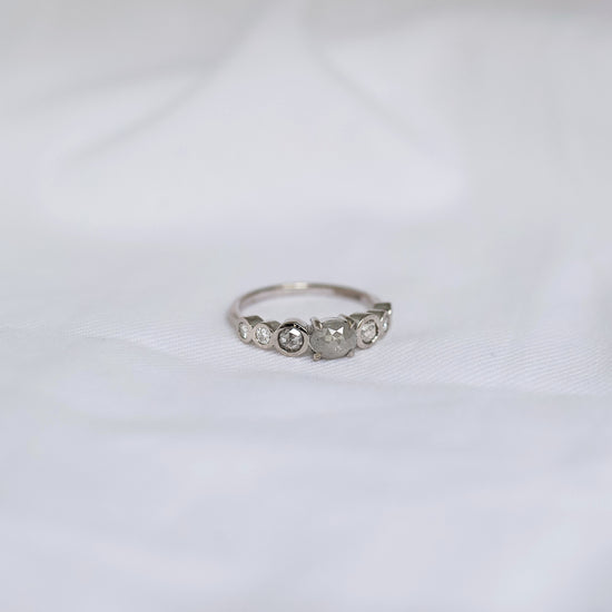 White Gold ring with small grey included diamonds on a white fabric background