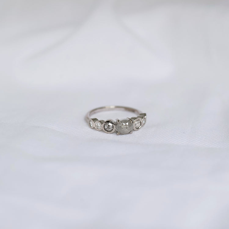 White Gold ring with small grey included diamonds on a white fabric background