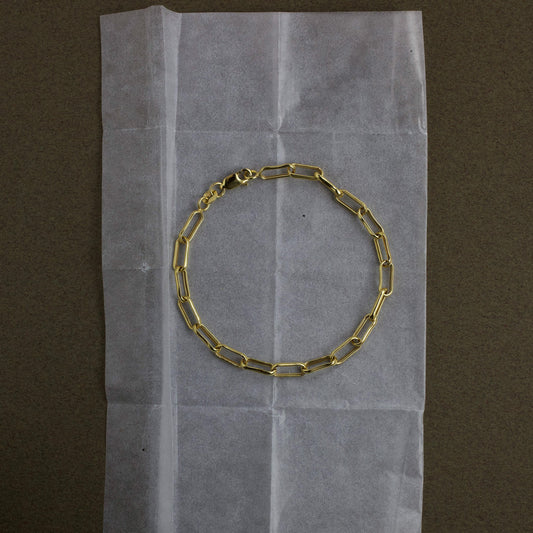 Gold chain bracelet on a piece of white paper with a brown background