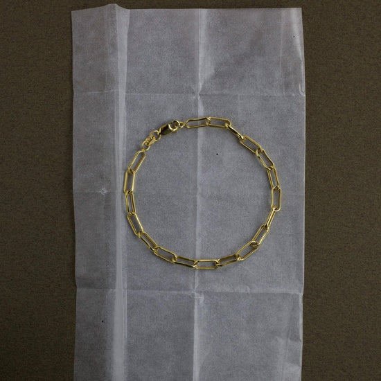 Gold chain bracelet on a piece of white paper with a brown background