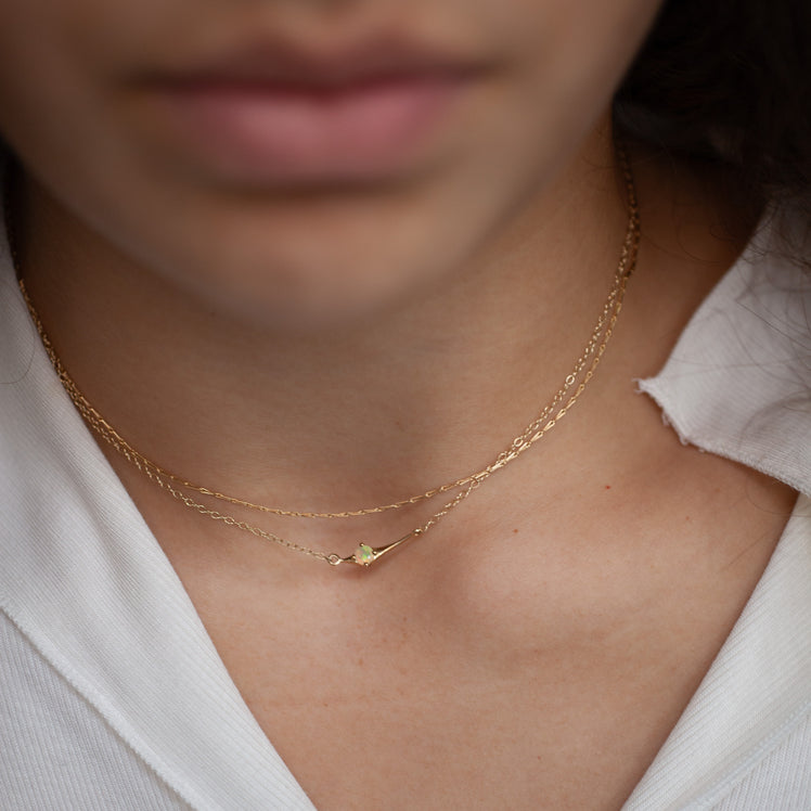 Close-up of a person wearing a gold necklace with a opal gemstone on a blurred background